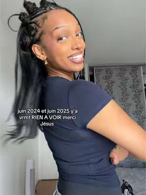 A woman with dark skin and braided hair smiles broadly toward the camera, with text overlaid on the image. She is wearing a dark blue t-shirt and a delicate gold earring. The background is a blurred out interior space, and the lighting appears natural.