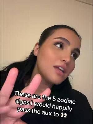 A woman with dark hair is looking toward the right side of the frame and speaking. Her right hand is up, displaying her fingers towards the camera. Text is overlaid on the bottom of the frame.