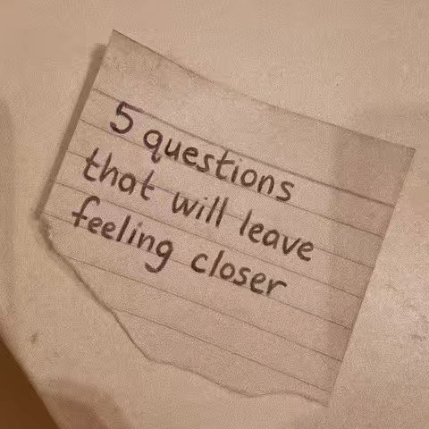 A piece of torn lined paper sits at an angle on a neutral surface. Handwritten in black marker are the words "5 questions that will leave feeling closer."