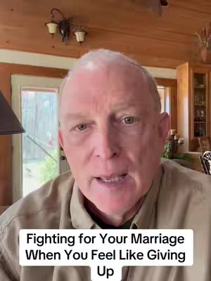 A man is shown in a well-lit indoor setting, likely his home, with a soft focus on his face. He has light skin, a bald head, and is wearing a light-colored shirt. A text overlay at the bottom reads, 'Fighting for Your Marriage When You Feel Like Giving Up'. The background includes wooden elements and a light fixture, suggesting a casual environment.