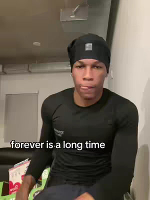 A man wearing a black beanie and a black long-sleeved top is the main focus of the image, positioned against a neutral indoor background. The composition has the man's face centered, set against a simple domestic scene. Text, 'forever is a long time' is below the man's face