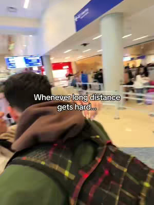 The image shows the back of a person in a green jacket and a plaid overshirt standing in an airport terminal. They are looking forward, with a sign and other people in the background. Text overlayed on the image says 'Whenever long distance gets hard...'.