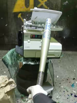 The image shows a white printer being hit with a baseball bat, causing it to break apart amid shattered glass and debris.