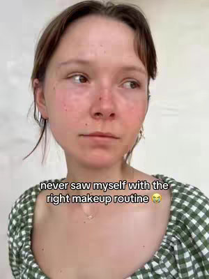 A young woman with fair skin is seen in a close-up shot, looking slightly off-camera with a thoughtful expression. She has light brown hair and is wearing a green and white checkered top. The background is a plain white wall. Text overlaid on the image reads, 'never saw myself with the right makeup routine.'
