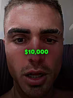 A close-up shot of a man's face. A green text overlay reads '$10,000' near the center of the frame, above the man's mouth. The man's skin has a slightly reddish tone, possibly from lighting or skin reflection. He has short, dark hair, a mustache, and is looking directly at the camera with a neutral expression