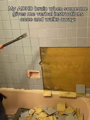 The image shows a bathroom being demolished. A person is holding a crowbar, prying tiles off a wall. The surrounding area is a mess, with debris on the floor.