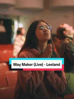 A woman with long dark hair wearing glasses and a brown hoodie is the central focus. Her hands are clasped in prayer in front of her face, and she has her eyes closed. A text overlay with the video title is placed on the bottom of the image, and the background shows a blurry church environment.