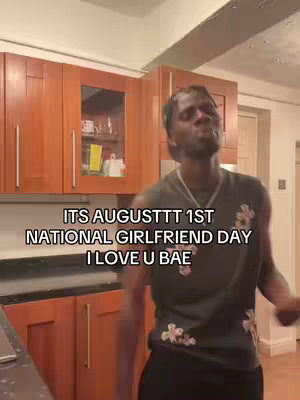 A man is dancing in a kitchen setting with text overlayed on the screen. The kitchen features wooden cabinets and appears to be a home kitchen. The man is wearing a dark t-shirt with white flower prints and a silver chain. The text in large font is easily readable.