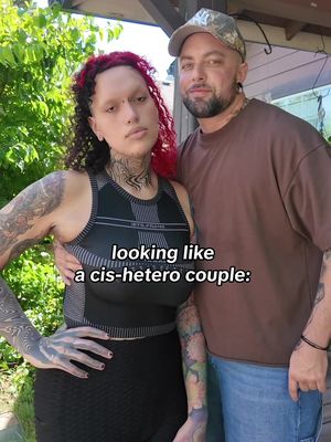 A photo of a couple posing closely together. One person has red curly hair and a detailed tattoo on their neck, wearing a black sports bra. The other person, male, is wearing a camouflage baseball cap and a brown shirt. The text overlay says “looking like a cis-hetero couple:”.