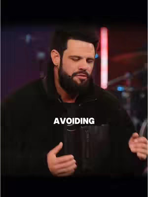 The cover image shows a medium shot of a man with a beard and dark hair. He is wearing a black jacket and looking down with a somewhat sorrowful expression. The word 'AVOIDING' is written in bold white font across the image.