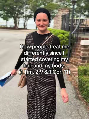 A woman in a black head covering and a modest black and white polka-dot dress is standing on a walkway. She is smiling slightly and looking towards the camera. The image features the woman in the foreground with a blurred outdoor setting in the background. Text overlay at the top of the frame describing the content.