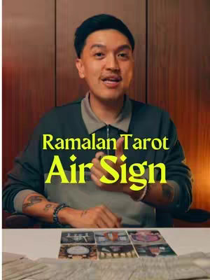 A man is in front of a wooden panel. He is wearing a dark green jacket over a light green shirt. Gold text overlays are visible. Underneath there is a white table with multiple tarot cards are laid out on the table.