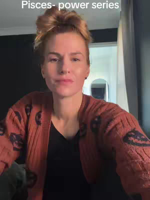 A woman with light skin and reddish hair, pulled back in a bun, sits in front of a dark background. She wears a rust-colored cardigan over a black shirt. The text overlay 'Pisces- power series' is at the top.