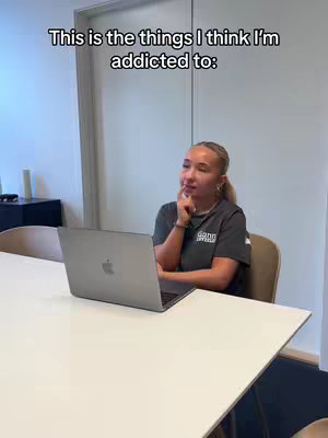 A woman sits at a table with a laptop, looking thoughtful. Text overlayed on the cover image says 'This is the things I think I'm addicted to:'.