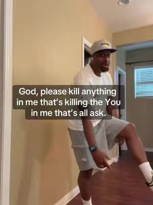 A man in a white t-shirt, gray shorts, and a baseball cap. The man is standing near a wall with a wooden door and a window at the back. The picture has overlays with text that says "God, please kill anything in me that's killing the You in me that's all ask."