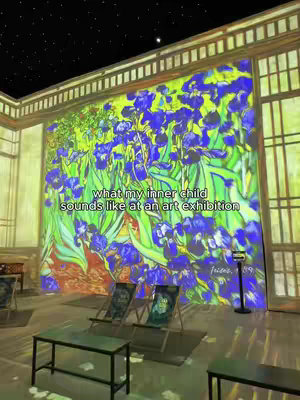 The image showcases an art exhibition with projected images, a large floral artwork in vibrant blues and greens dominating the main wall. The foreground features benches and chairs arranged for visitors and text over image reveals the theme related to art appreciation, with hints like stars projected in the night's sky.