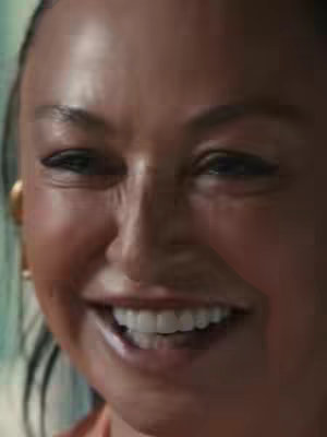 A close-up shot focusing on the face of a woman smiling widely. The background has a slight greenish tint.