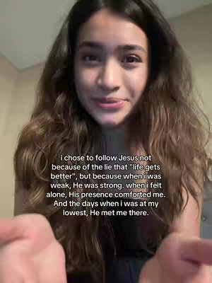 A woman with long, wavy brown hair is centered in a selfie-style video. Her expression is gentle and inviting. The background is a neutral, light-colored wall. The text overlay includes a reflection on faith, starting with the phrase, "i chose to follow Jesus."