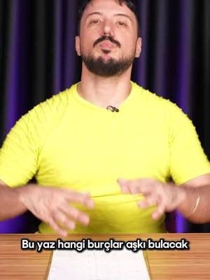 A man with a beard and mustache wearing a yellow shirt, speaking directly to the camera with his hands raised. The text overlay at the bottom says 'This summer which zodiac signs will find love'. The background includes a purple drape and a wooden table in the bottom.