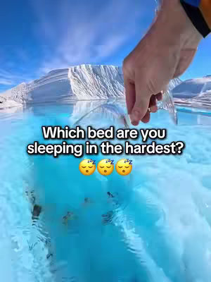 An aerial view of a person's hand dipping a cup of clear water into a stunning turquoise body of water. The background features an icy mountain with a vivid blue sky.