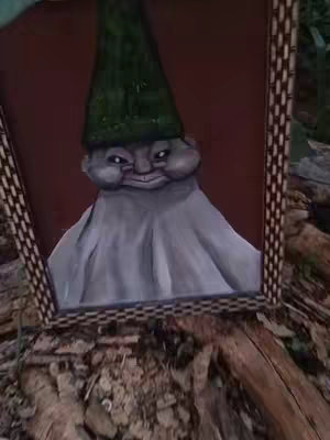 The image shows a framed painting of a gnome-like creature. The creature has a grey face with puffy cheeks and a slightly evil grin, wearing a dark green hat. The painting is set within a dark wooden frame and is placed on a textured surface, possibly a tree stump, which is in a slightly blurred background.