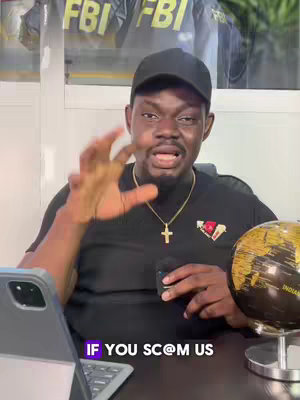 A man in a black cap and shirt is facing the camera, gesturing with his right hand. Behind him are blurry FBI logos, and a globe and laptop are positioned on a desk. Text overlayed in a purple rectangular box at the bottom of the screen says 'IF YOU SC@M US'.