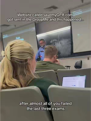 A classroom setting with a blonde woman in the foreground facing away from the camera. She is seated in a desk chair with a laptop open on the desk. In the background, a professor with glasses is standing near a projection screen, while another student is seated in a desk in between. Additional text overlays the image.