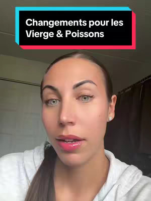 A selfie-style video cover featuring a woman with light skin, pale eyes, and dark hair pulled back. She wears a white hoodie and red lipstick. Above her is a teal and red banner with white text. The background is a neutral wall and some dark clothing items.
