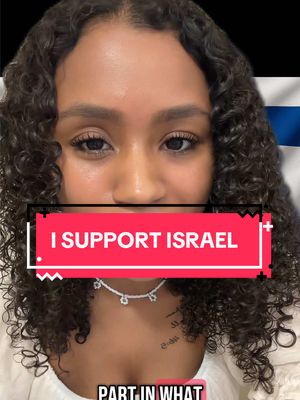 A woman with curly dark hair is centered in the frame. She is wearing a white top and a delicate necklace. The background includes a section of the Israeli flag. Across her chest is a red rectangle with the text 'I SUPPORT ISRAEL'.