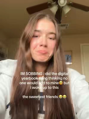 A young woman with long brown hair is centered in a selfie-style video. She has a slightly pained or emotional expression, with a slight pout. The background is a warm, beige-colored room with a ceiling fan. Overlaid text mentions a yearbook and the sentiment "the sweetest friends".