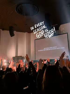 The cover image shows a large group of people with their hands raised in what appears to be a church or concert setting. A screen in the background displays text, and there is overlay text on the image. The lighting is warm, with a focus on the stage area.