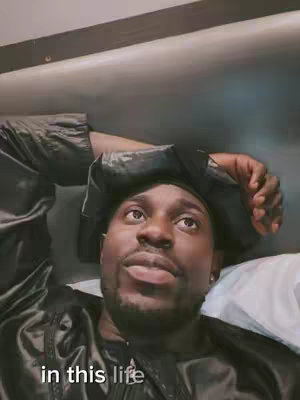 A man is lying down, propped on a bed. The man's face is turned upwards, eyes looking up. The text overlay 'in this life' is at the bottom of the visual.