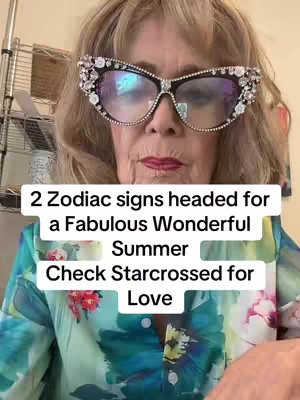 The image shows a woman wearing large, bejeweled eyeglasses against a background that appears to be a floral-patterned blouse. The woman has light blond hair and is looking directly at the camera with a partially visible room in the background.