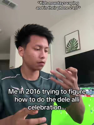 A young man in a dark green shirt is the main focus, indoors. He is looking down with a thoughtful expression, his fingers held up as if miming a sports celebration. Above him is text that reads, "*Kids nowadays vaping and in their phone 24/7*". Below the image are the words "Me in 2016 trying to figure how to do the dele alli celebration..." The background includes a wall, a framed image, and a television, which is displaying what appears to be a soccer match.