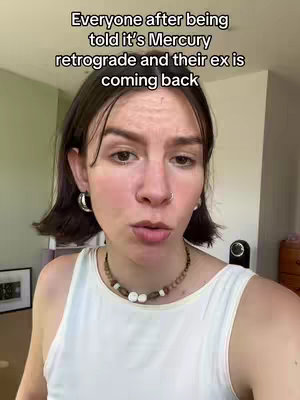 A medium shot shows a woman with short dark hair, a white top, and a beaded necklace talking to the camera. The image has text in a white box overlayed above the woman's head.