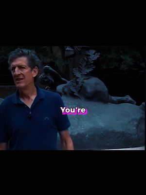 The image shows a man in a blue polo shirt standing in an outdoor setting, with a blurred statue in the background. The image is framed from the waist up, with the man positioned slightly to the left. Text overlayed on the image reads "You're" in a pink and white font.