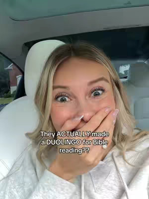A blonde woman is inside a car, covering her mouth with her hand in a surprised expression. The text overlay reads, “They ACTUALLY made a DUOLINGO for Bible reading??”.