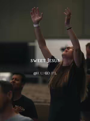 A woman with long, light brown hair raises her arms towards the ceiling. She wears a dark-colored shirt. The text "SWEET JESUS" is overlaid in a bold white font with the handle "@HOLY GO PL" below it.