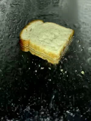 An overhead shot of a slice of bread submerged in water which is creating motion and streaks, with slight yellow tinges showing the bread's freshness.