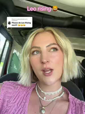 A woman with blonde hair in a light pink top is sitting inside a vehicle. A text overlay, "Leo rising" with a lion emoji appears on the upper part of the image. A comment appears to the left of the woman: "Please do Leo Rising next!!" There are multiple necklaces on the woman's neck.