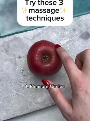 The image shows a red apple on a marble or stone textured surface. The top of the image features text in a white box against a solid background, with an additional overlay of text labeling a massage technique. A hand with red nail polished fingers enters the frame from the side, touching the apple.