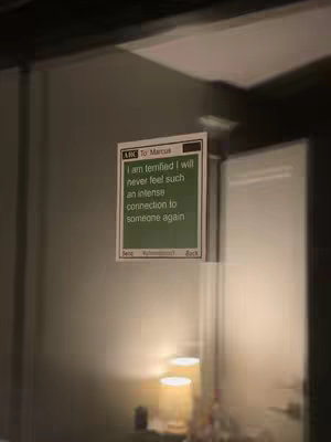 A dimly lit room with a glass door on which a note is attached. The note appears to be a digital sticky note with the text in a bold font. The composition has an intimate and personal feel with a warm, blurred light source in the background.