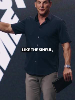 A man in a dark blue short-sleeved shirt and gray pants is standing on a stage, holding a book. Text overlayed on image.