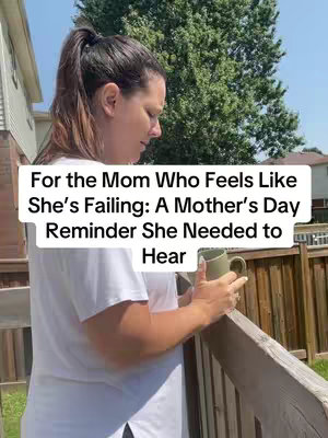 A woman with dark hair pulled back is seen from the side, looking down with what appears to be a sad or thoughtful expression. She is wearing a white t-shirt and holding a green mug. She is standing on a wooden deck. The background consists of a fence, trees, and part of what looks like a building.