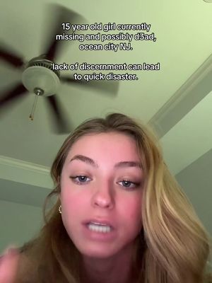 A selfie-style video cover image with a young woman centered, slightly blurred. The background shows part of a ceiling and a ceiling fan. Overlayed text in the upper-left corner provides a somber message about a missing person. The woman has blonde hair, and a serious expression as she speaks.