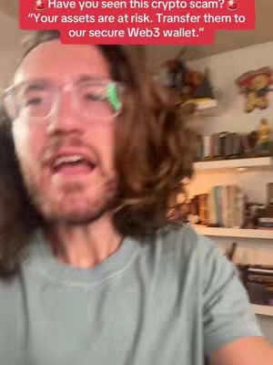 A man with long brown hair and glasses is speaking directly to the camera. Above him is a red banner with white text warning of a crypto scam. The background is slightly blurred, showing a room with bookshelves.