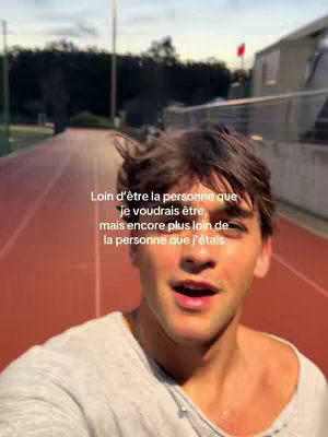 A young man filming himself as he walks towards the camera on a track. The background is blurred, suggesting a sunny outdoor setting. Text is overlaid, and the man appears to be speaking.