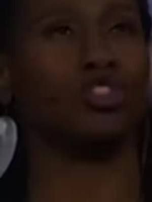A close-up shot features a dark-skinned person with a dark background. The person's face is the main focus. Their eyes are looking up, and their lips are slightly parted, as if they are about to speak. The lighting is dim, with the face emerging from the darkness.