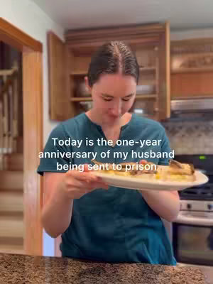A woman in a teal shirt stands in a kitchen, holding a plate of food. Text overlaid on the image says, "Today is the one-year anniversary of my husband being sent to prison."