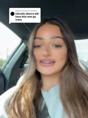 A woman is filmed from the chest up, inside of a car. She has long, light brown hair, and is wearing a light colored top. The background shows the interior of a car. A speech bubble in the top left corner contains text.